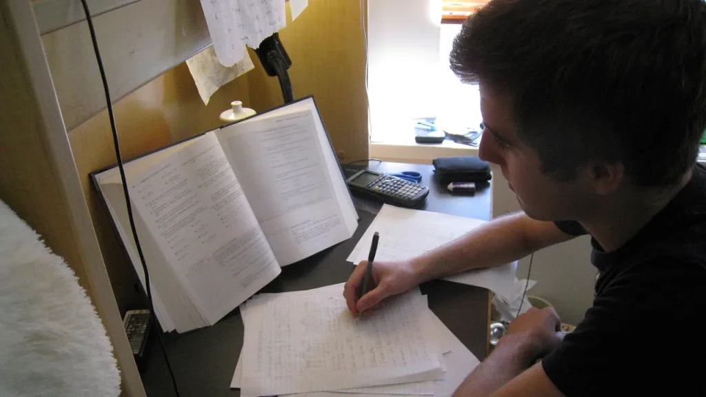 Pessoa estudando com livro, anotações e calculadora para ilustrar banco de questões para concurso