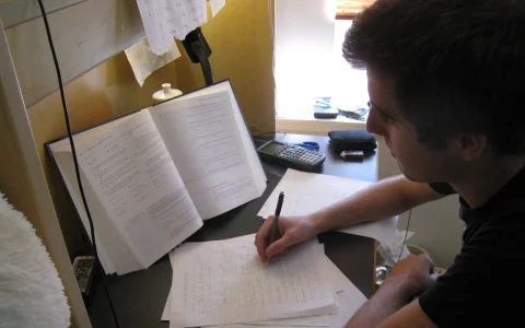 Pessoa estudando com livro, anotações e calculadora para ilustrar banco de questões para concurso